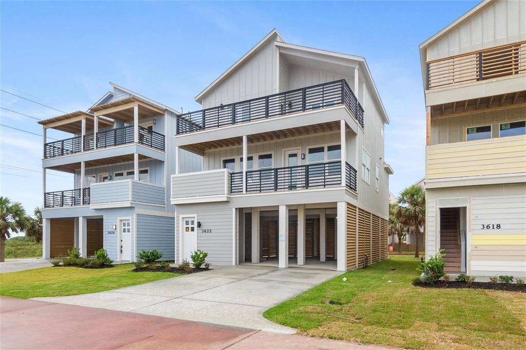 Multi-story home featuring a light gray exterior with black trim and balconies, offering a spacious car ports and a fresh coastal vibe.