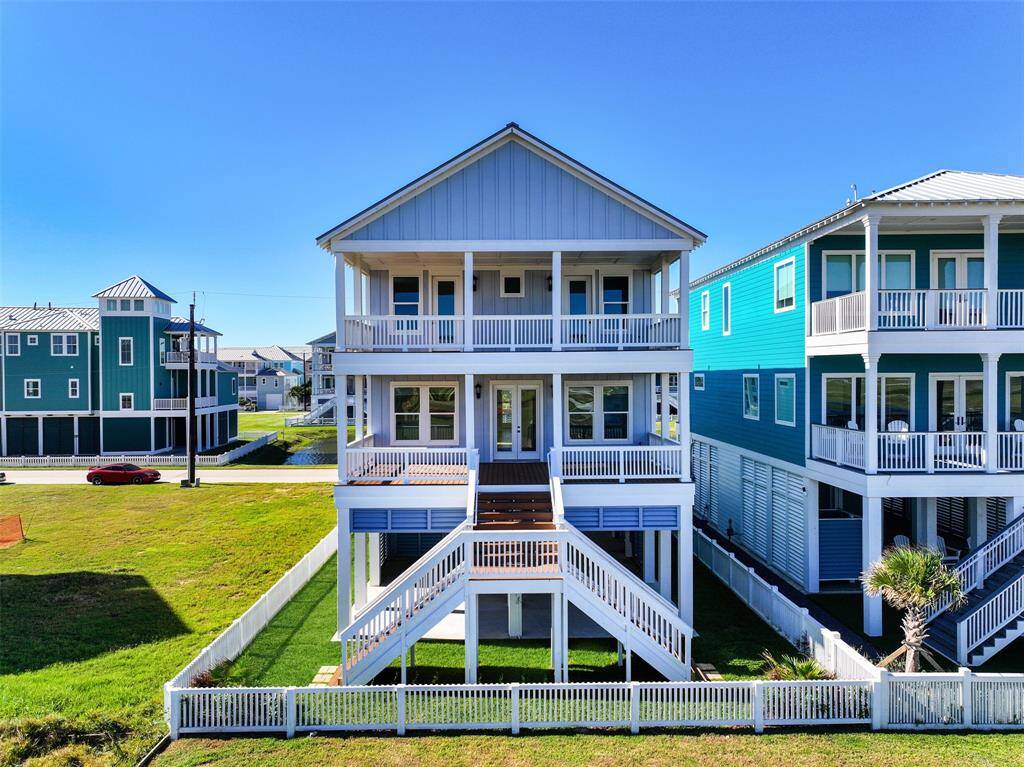 This back view showcases the home’s impressive three-level design, complete with a grand dual-sided staircase leading from the main floor to the ground level. The fenced-in backyard provides privacy and the perfect space for outdoor enjoyment.