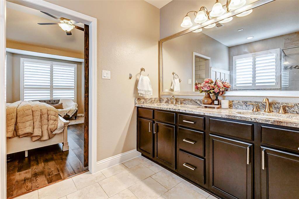 Welcome to your primary bathroom! It features a spacious vanity with dark cabinetry, granite countertops, and dual sinks. You'll also find a framed mirror and an updated lighting fixture, adding a modern touch to the space.