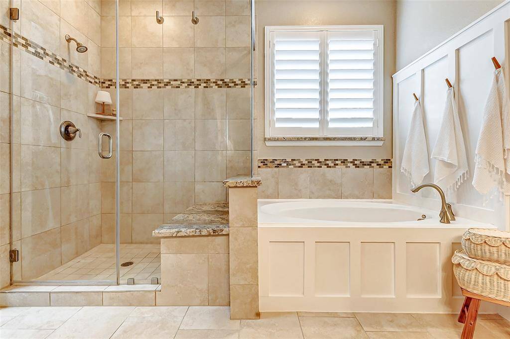 The accentuated soaking tub is positioned beneath a large window with plantation shutters, allowing natural light to fill the space while maintaining privacy. Additionally, an accent wall with built-in hanging hooks adds both style and functionality to the room.