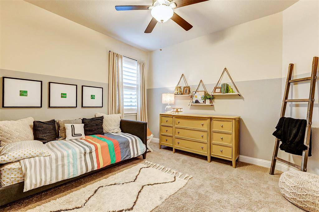 This guest room is beautifully enhanced with accent paint on each wall, complemented by plush carpeting, a ceiling fan, and a large window adorned with plantation shutters.