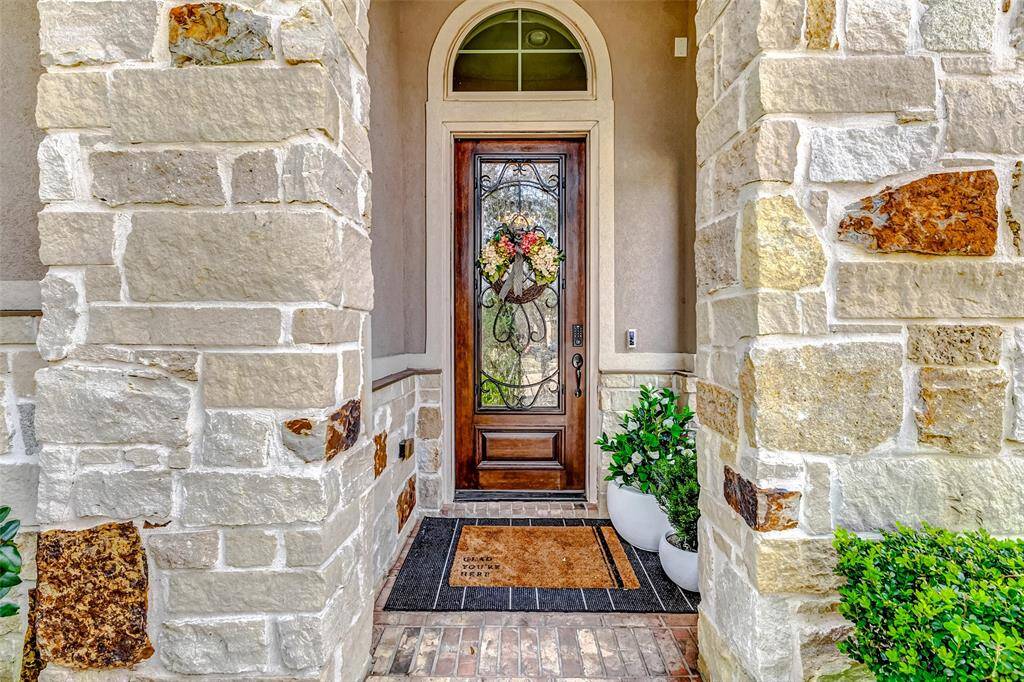 Follow the landscaped pathway to your inviting front porch, showcasing natural stone and a stunning front door with an elegant glass inlay.