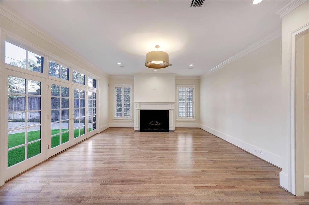Family Room with floor to ceiling windows, French Doors, recent windows, refinished hardwood floors, and centered by a gas log fire place & decorative lamp shade pendent. Opens to the Kitchen, with doors leading to the garden.
