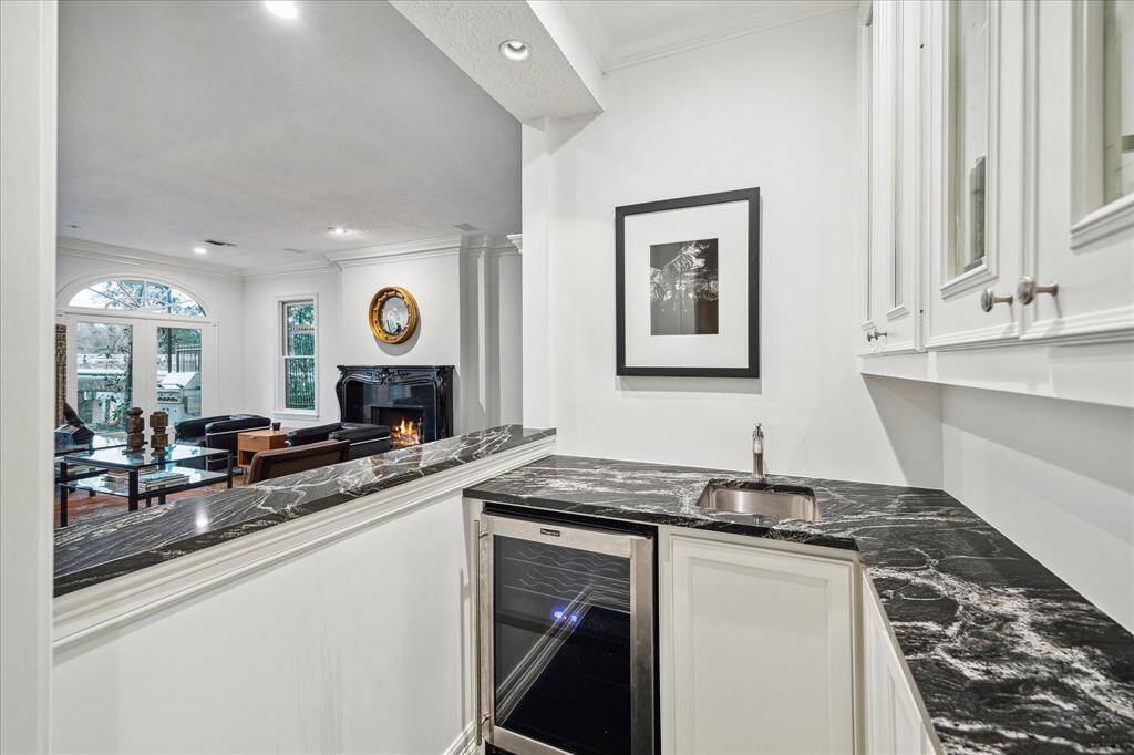 WET BAR - Perfect for entertaining, the wet bar features sleek black quartz countertops, a stainless steel bar sink, and a Magic Chef beverage refrigerator. Upper glass-front cabinetry provides elegant display space while lower cabinets offer ample storage.