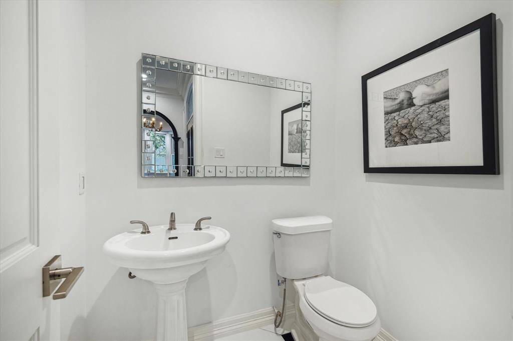 POWDER ROOM - A sophisticated powder bath features a pedestal sink, black-and-white diamond-pattern tile flooring, and an Art Deco mirror. Double crown molding and recessed lighting complete the elegant design.