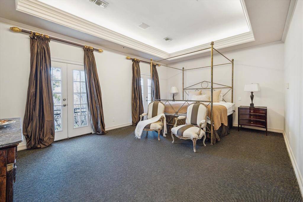 PRIMARY BEDROOM - This serene retreat boasts dual sets of French doors opening to Juliet balconies, filling the space with natural light. A tray ceiling with soft accent lighting and custom window coverings enhances the luxurious atmosphere.