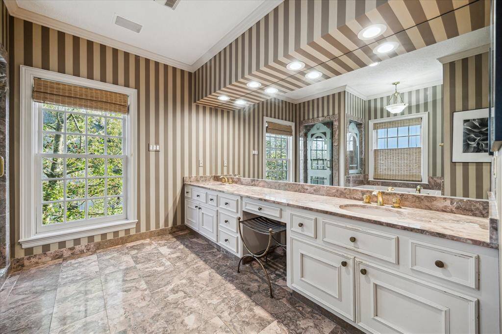 PRIMARY BATHROOM - A dual vanity with marble countertops, polished brass fixtures, and a Jacuzzi jetted bathtub offers the ultimate relaxation. Counter-to-ceiling mirrors enhance the sense of space and light.