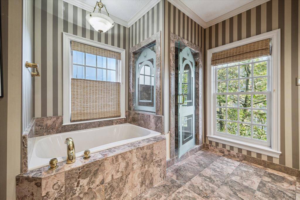PRIMARY BATHROOM -Marble finishes, an alabaster chandelier, and a custom walk-in shower with John Meek Design Studio glass create a spa-like retreat. A built-in linen cabinet and woven wood window treatments add both style and function.