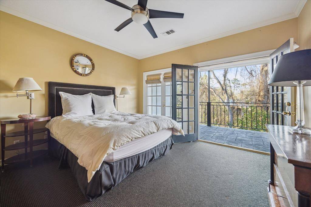 GUEST BEDROOM #1 - French doors open to a private second-floor balcony, allowing fresh air and natural light to fill the room. Soft carpet flooring, a ceiling fan, and custom window coverings create a comfortable and stylish space.