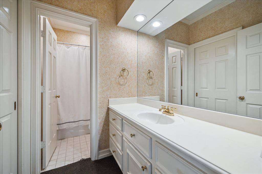 GUEST BATHROOM #1 - A Kohler tub/shower combination, brass fixtures, and a sleek neutral vanity blend luxury with practicality. Designer wallpaper and crown molding add a refined touch.