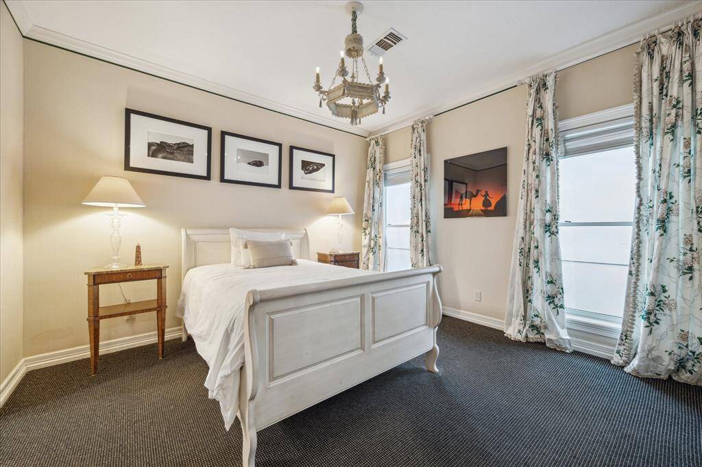 GUEST BEDROOM #2 - This inviting guest suite features dual eastern-facing windows, soft neutral carpeting, and designer wallpaper. Crown molding and an antique chandelier complete the refined ambiance.