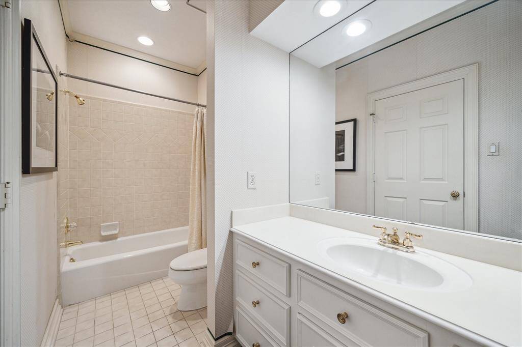 GUEST BATHROOM #2 - A well-appointed ensuite bath includes a neutral countertop with an integrated sink and brass plumbing fixtures. A classic Kohler tub/shower combination is complemented by timeless tile flooring.