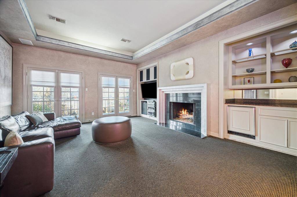 GAMEROOM - The expansive game room features a silver leaf gaslog fireplace and built-in cabinetry for media storage. Dual French doors open to a private balcony, creating a seamless indoor-outdoor flow.