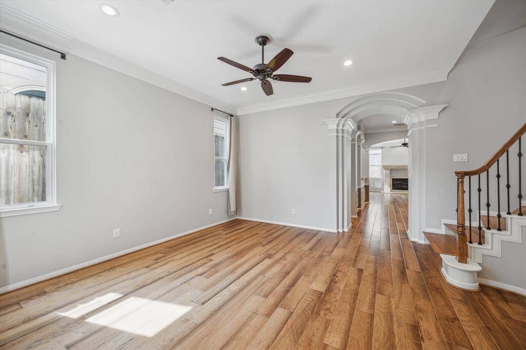 The formal living room is filled with natural light, which beautifully highlights the rich wood floors and adds warmth and elegance to the space. A stunning staircase serves as a focal point, adorned with exquisite wood and iron spindles, enhancing the room's sophisticated ambiance.