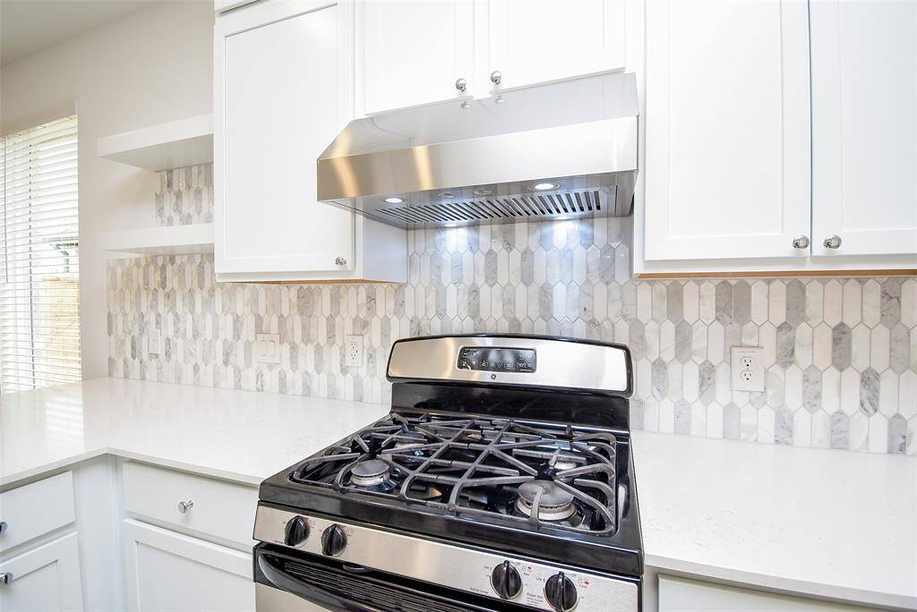 Gas range with oven below and lighten vent above.  Modern cabinets and open shelving.