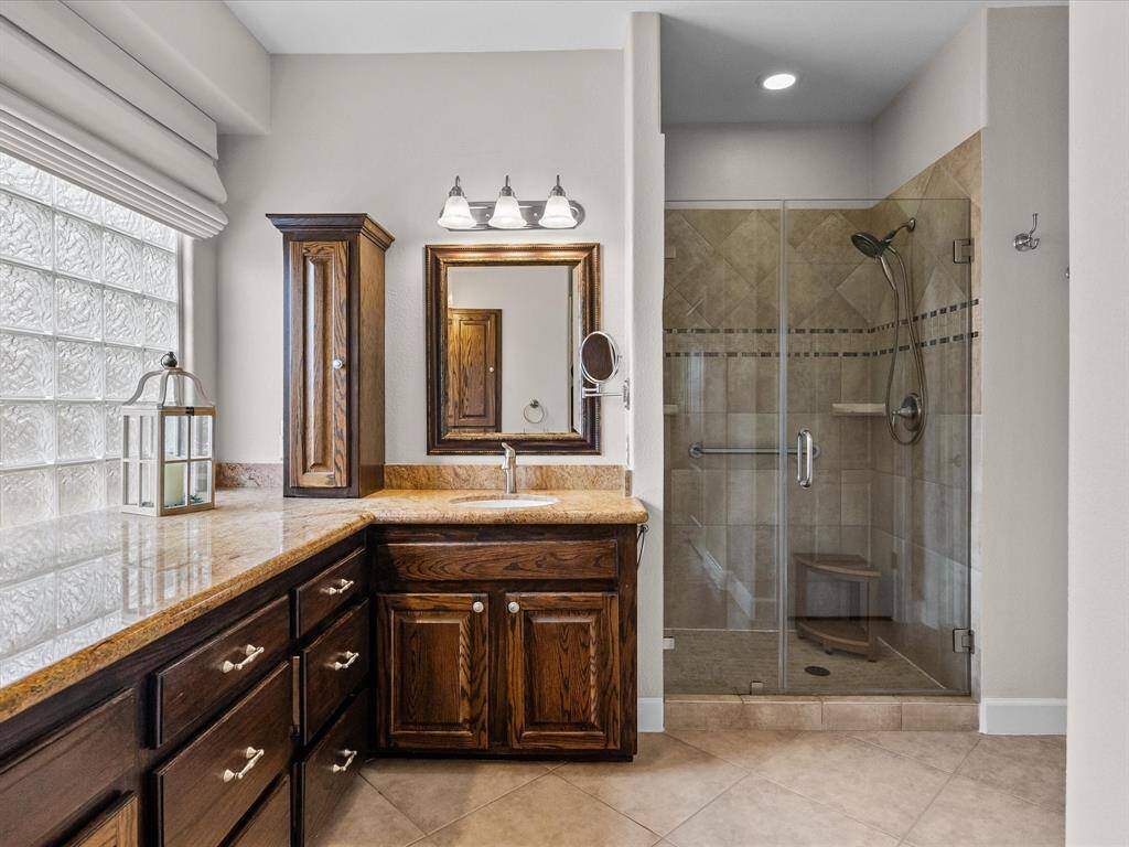 En-suite has a walk-in shower with tile surround, a vanity with ample storage, and a glass block window for natural light. This space offers a blend of functionality and style