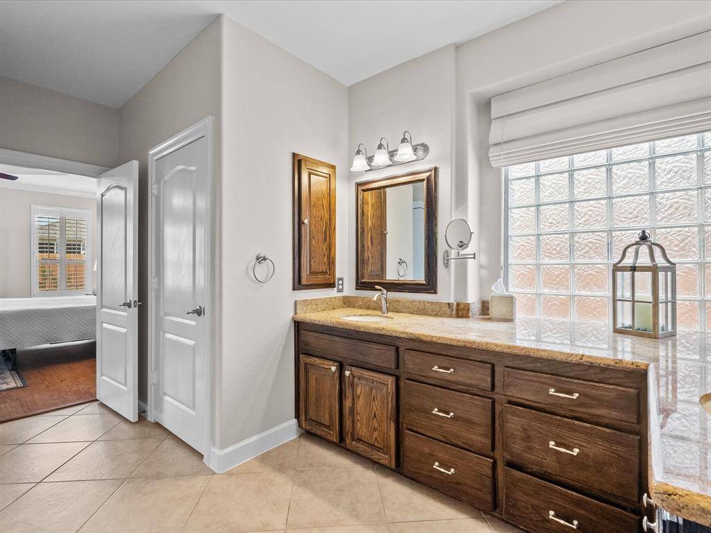 The primary en-suite, featuring tile flooring, a vanity with ample storage, and a glass block window for natural light.