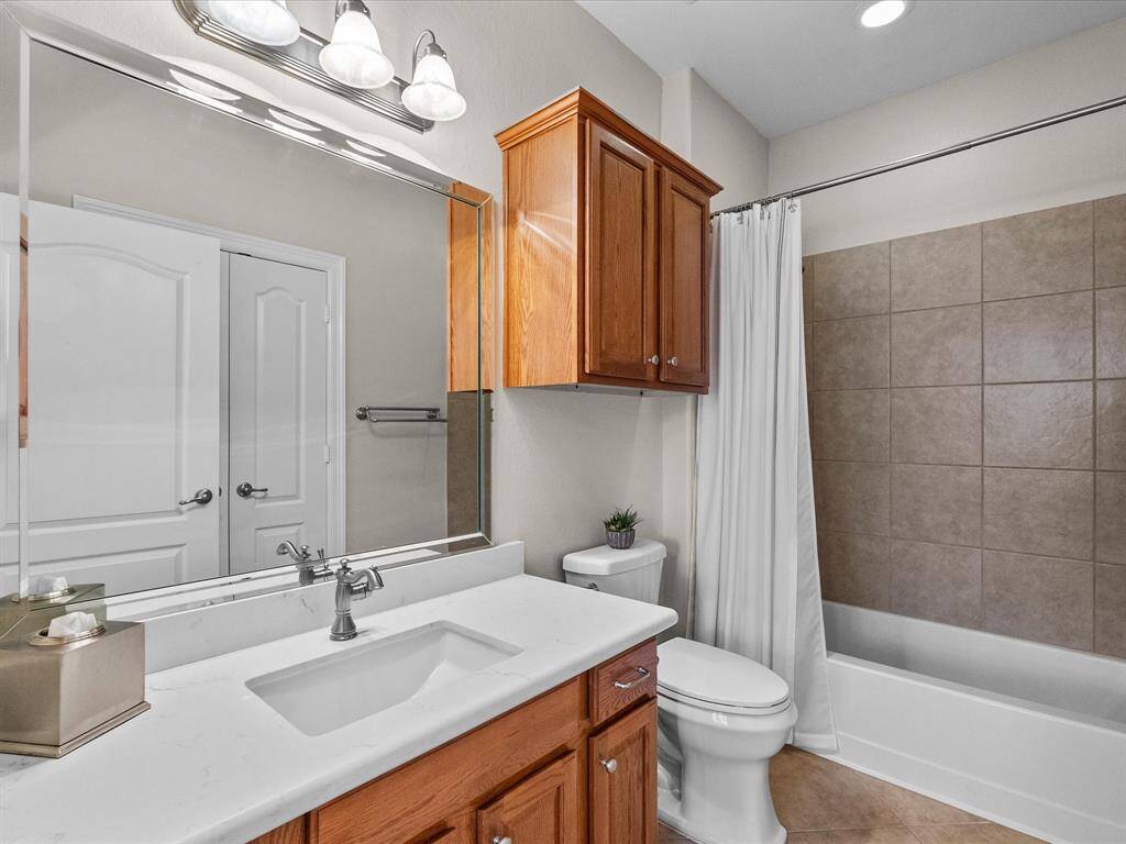 Guest bathroom featuring a vanity with quartz countertop, tile flooring, and a shower/tub combination. This bathroom offers functionality and convenience for guests.