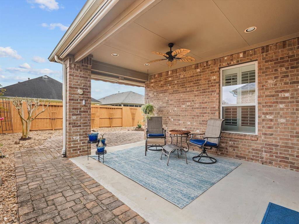 Covered patio with ceiling fan, providing a shaded outdoor living space. The paver walkway leads to a private, fenced backyard, perfect for relaxing and entertaining.