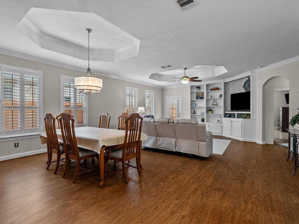 Open-concept living and dining area featuring LVP flooring, tray ceilings, and custom built-in shelving. This space offers ample room for entertaining and relaxation.