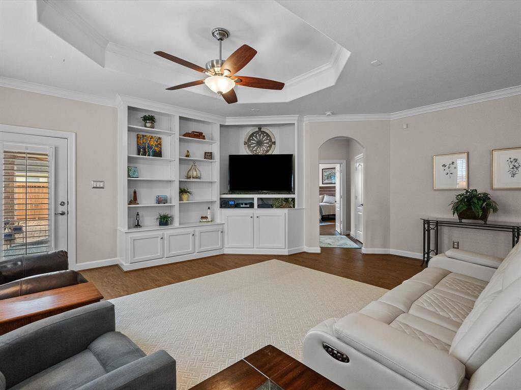 Comfortable living area featuring custom built-in shelving, LVP flooring, and a tray ceiling with a ceiling fan.