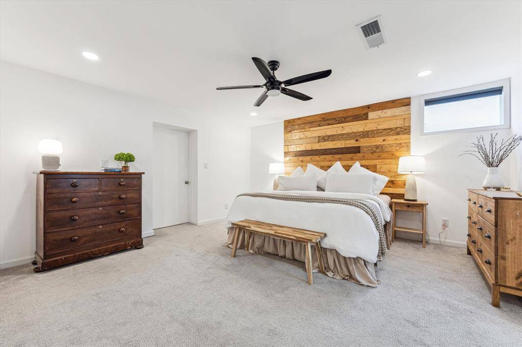 The spacious Primary bedroom features a cozy aesthetic with a wood accent wall, neutral carpeting, a ceiling fan, and a walk-in closet.