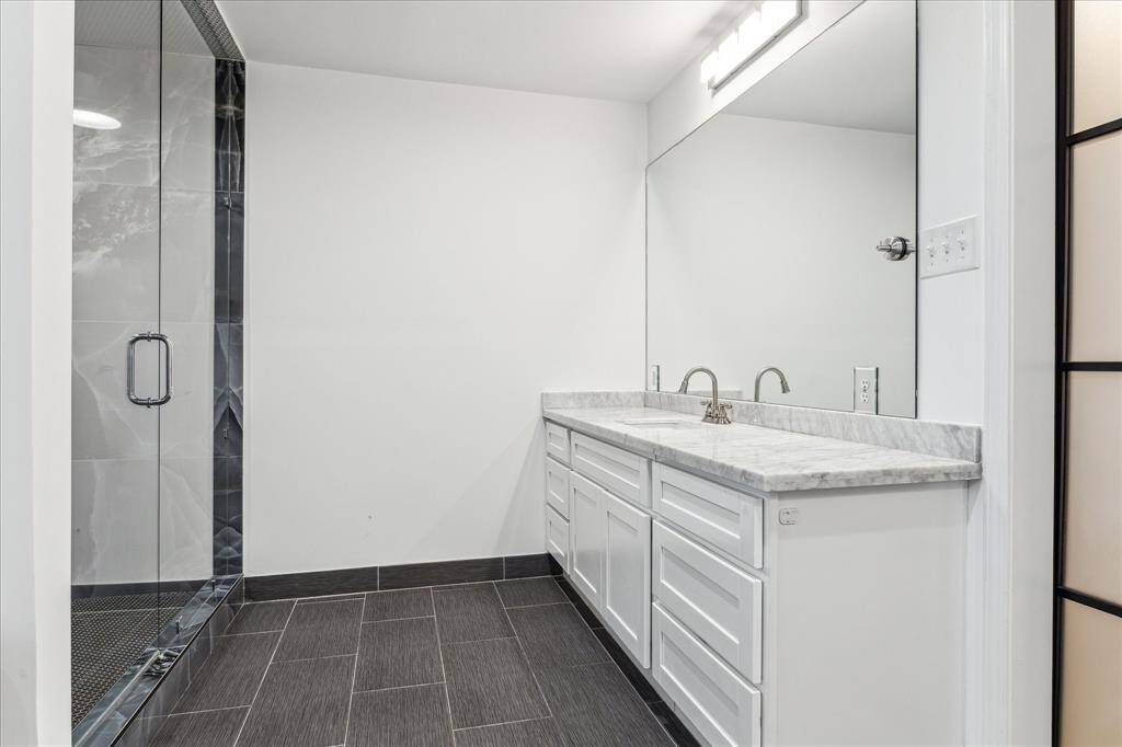 The spacious primary bathroom features a modern design with a spacious walk-in shower, sleek gray tile flooring, and a large vanity with marble countertops and ample storage.
