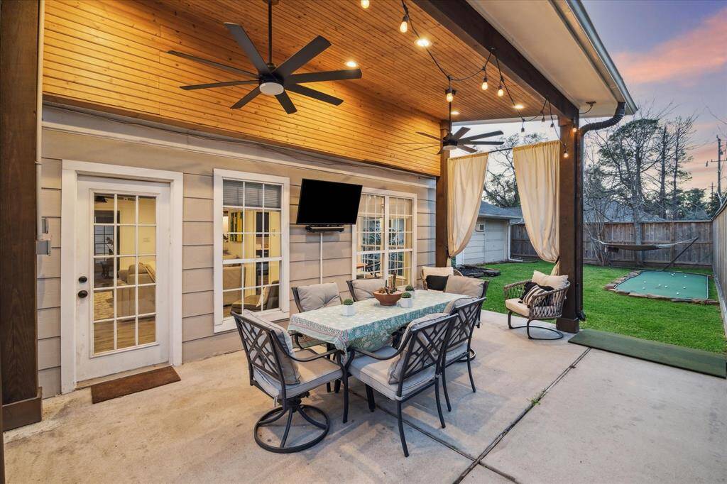 The inviting recently added outdoor patio features a cozy dining area with cushioned seating, ceiling fans, and string lights. It opens to a well-maintained yard with a putting green and hammock, perfect for relaxation and entertainment.