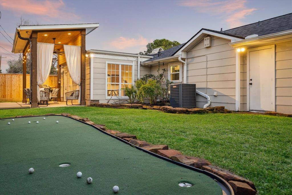 The backyard offers a well-maintained lawn, a putting green, and a covered patio area with seating, perfect for outdoor relaxation and entertainment.