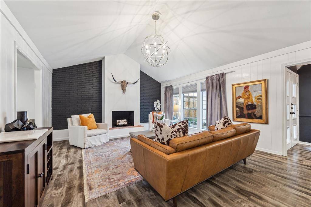 The living room features a cozy fireplace with a black accent wall, a vaulted ceiling, and abundant natural light from large windows. It has a chandelier offering a warm and inviting atmosphere.
