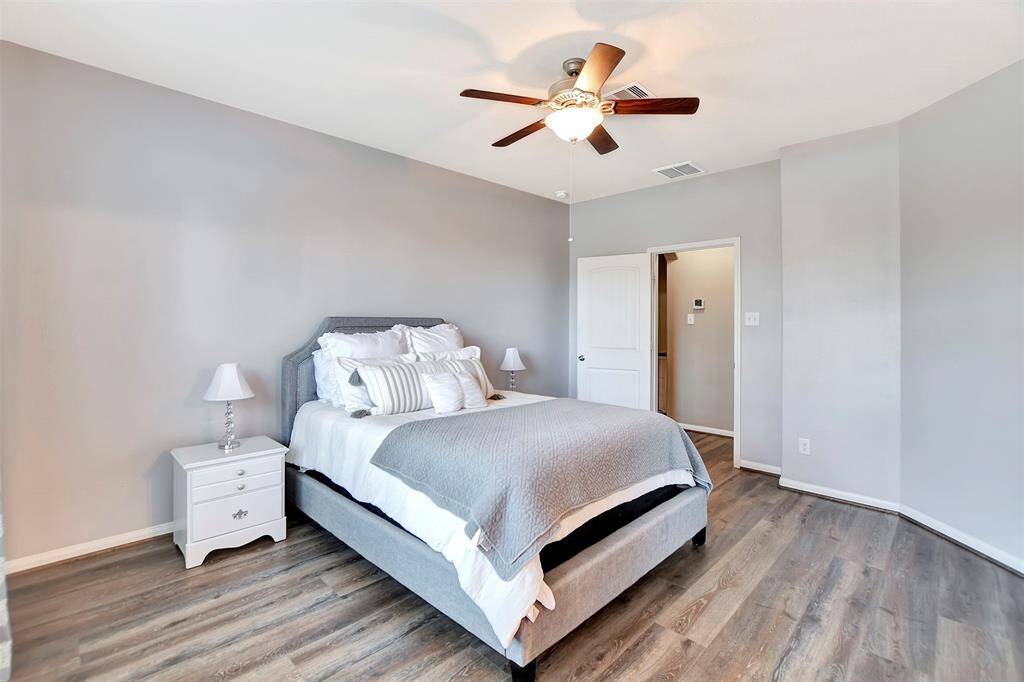 This bedroom has a neutral color palette with light gray walls and vinyl plank flooring. It includes a ceiling fan.