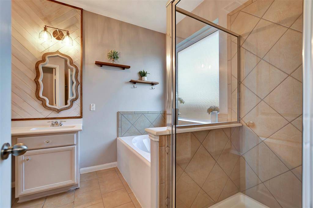 The primary bathroom features a stylish vanity with a decorative mirror, a spacious bathtub, and a glass-enclosed shower. Neutral tile and soft lighting create a warm, inviting atmosphere.