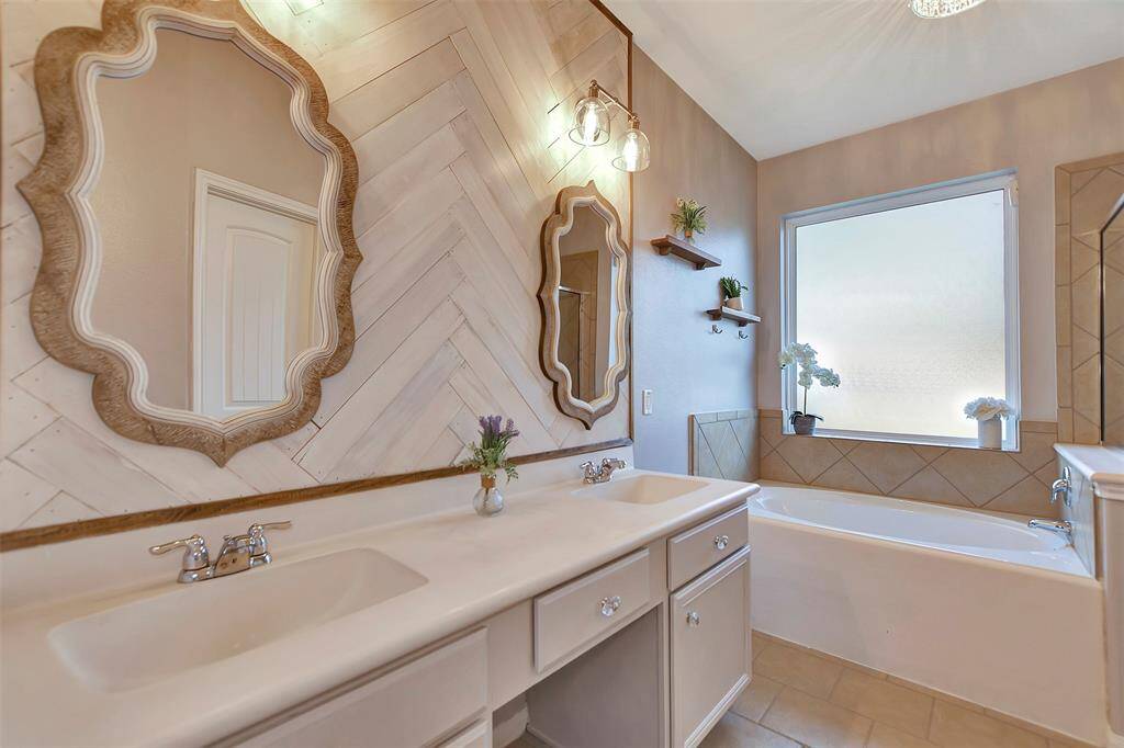 This bathroom features a dual-sink vanity with elegant mirrors. The chevron-patterned wall adds a stylish touch, complemented by modern lighting.