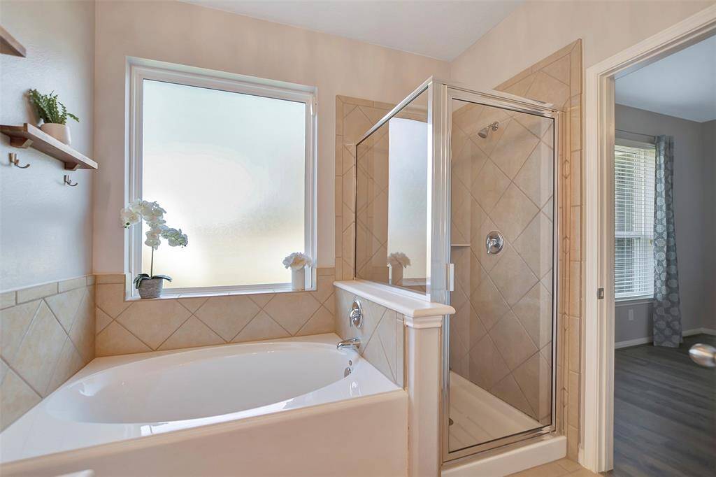This bathroom features a spacious soaking tub and a separate glass-enclosed shower, with tiled walls and a frosted window for privacy.