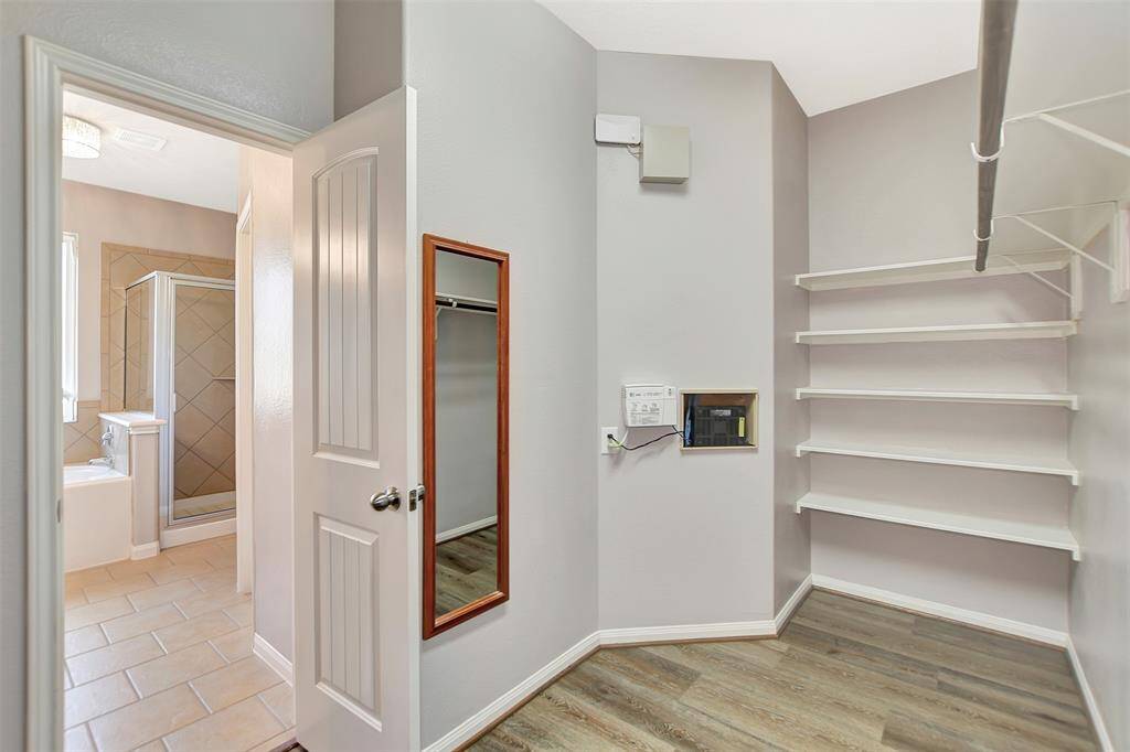 The walk-in closet has ample shelving and hanging space, adjacent to the primary bathroom. The closet has a wall-mounted mirror and a control panel, and the space is well-lit.