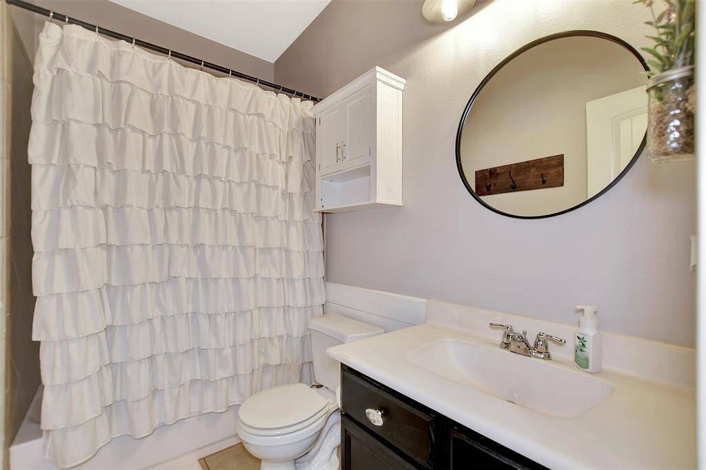This bathroom features a sleek round mirror and a stylish black vanity. A wall-mounted cabinet provides additional storage, and neutral tones create a clean, inviting atmosphere.