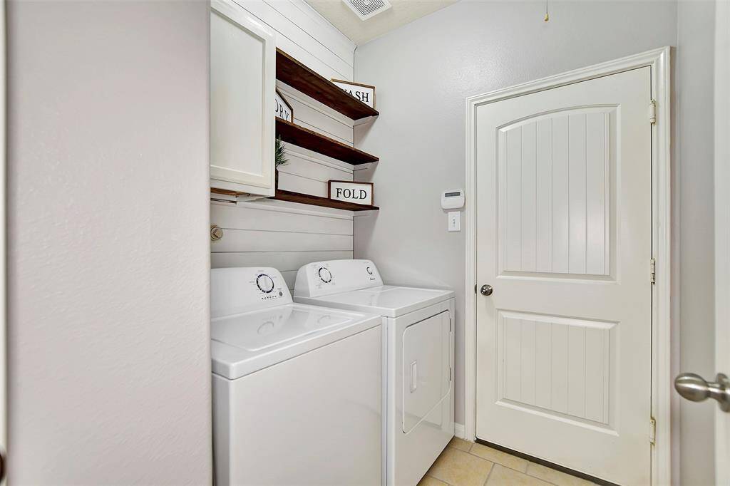 The laundry room has open and closed shelving for storage, and a neutral color palette. The space is well-organized with a decorative shiplap wall.
