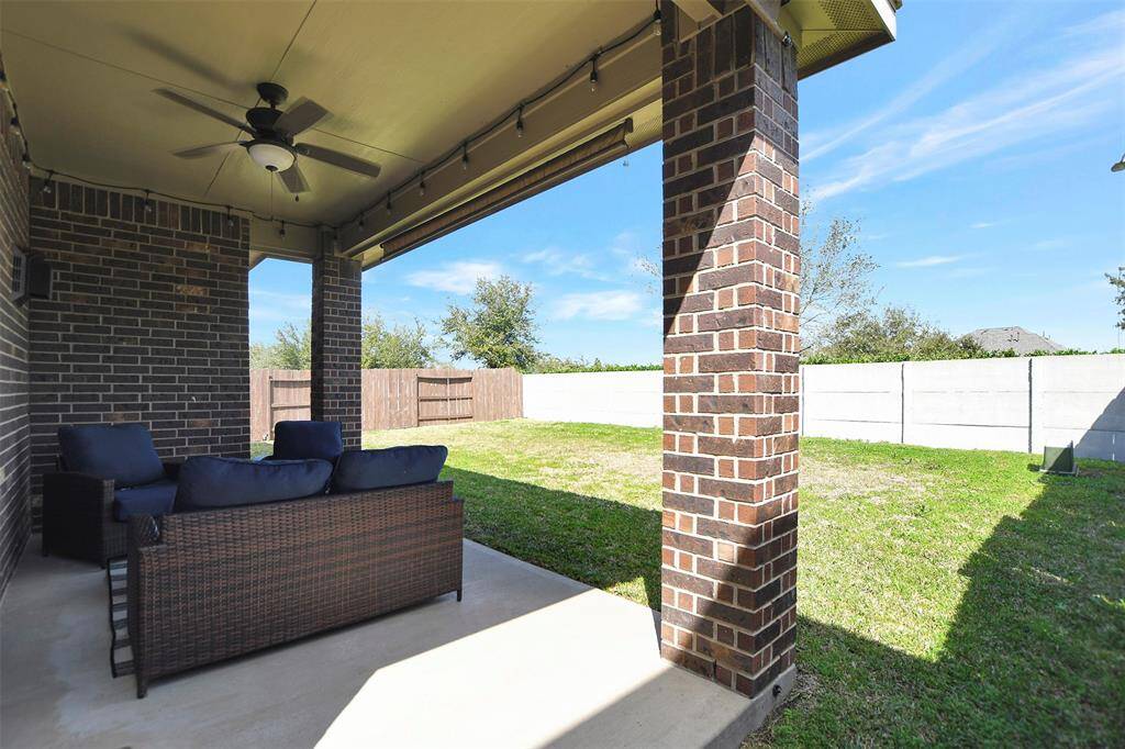 This photo showcases a covered patio with a ceiling fan, overlooking a spacious fenced backyard with a well-maintained lawn. Ideal for outdoor relaxation and entertainment.