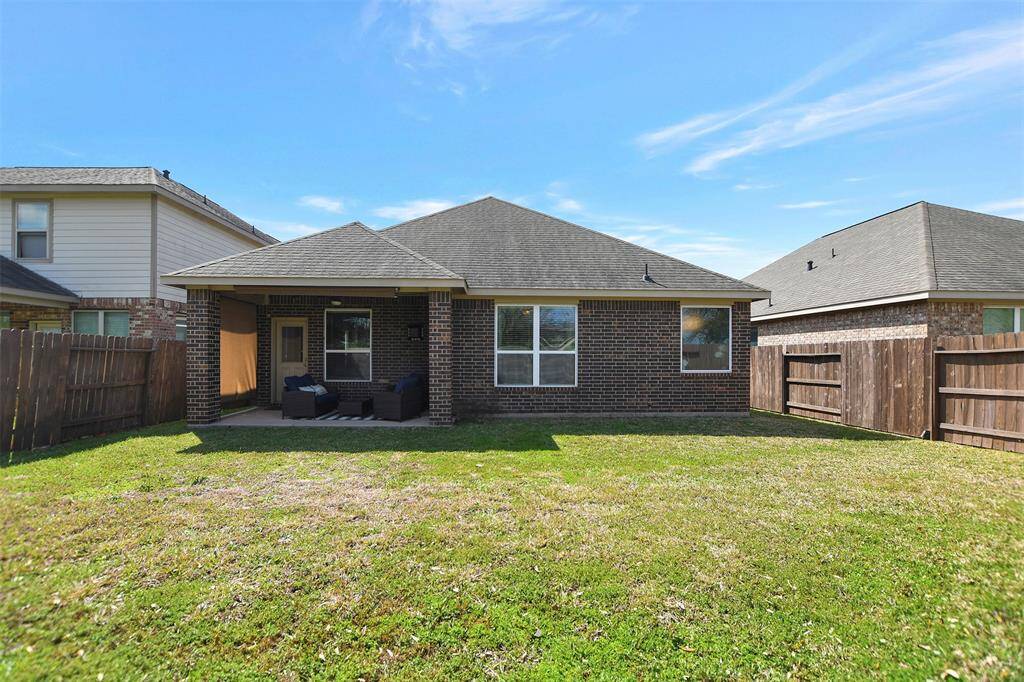 This photo shows the backyard of a brick house, featuring a covered patio area with outdoor seating. The yard is fenced and has a grassy lawn, offering a private space for relaxation or entertaining.