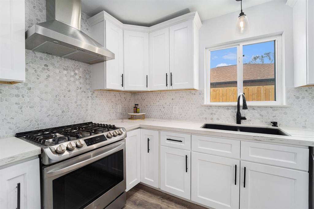 Stainless steel 5 burner gas range with a contemporary hood. Hexagonal tile backsplash, a black sink & faucet, and a seemsless quarts counter top.