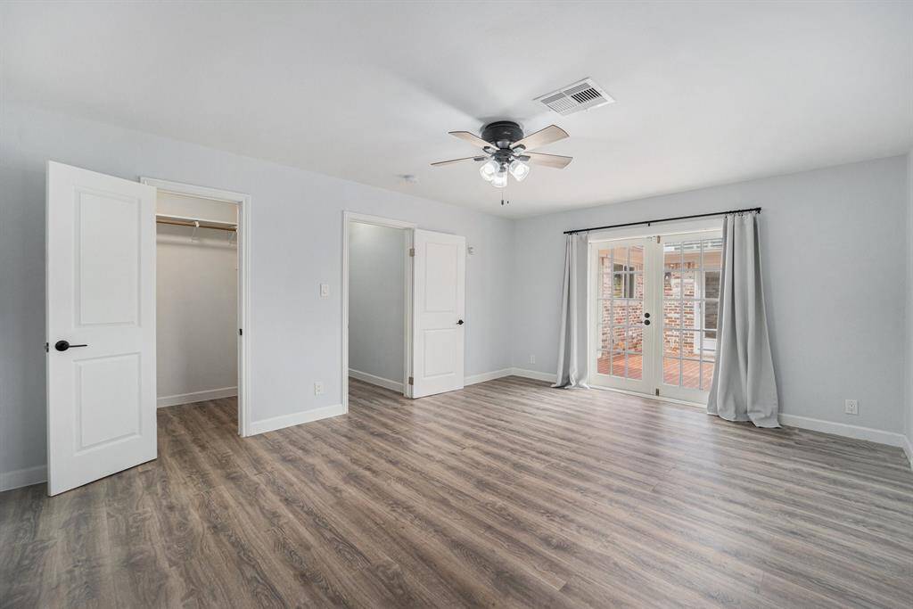 Spacious bright master bedroom, and French doors leading to a patio. Features a walk-in closet and neutral walls for a modern feel.