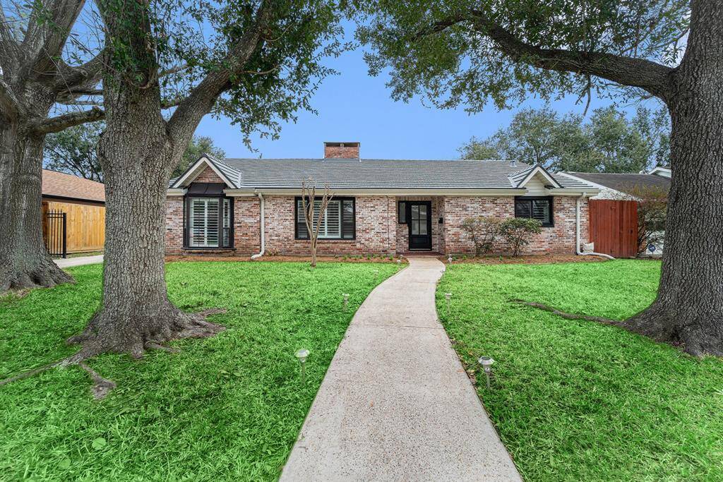 Charming single-story brick home with a welcoming pathway, framed by mature trees. Features a cozy front porch and modern windows. Ideal for comfortable living with a classic exterior.