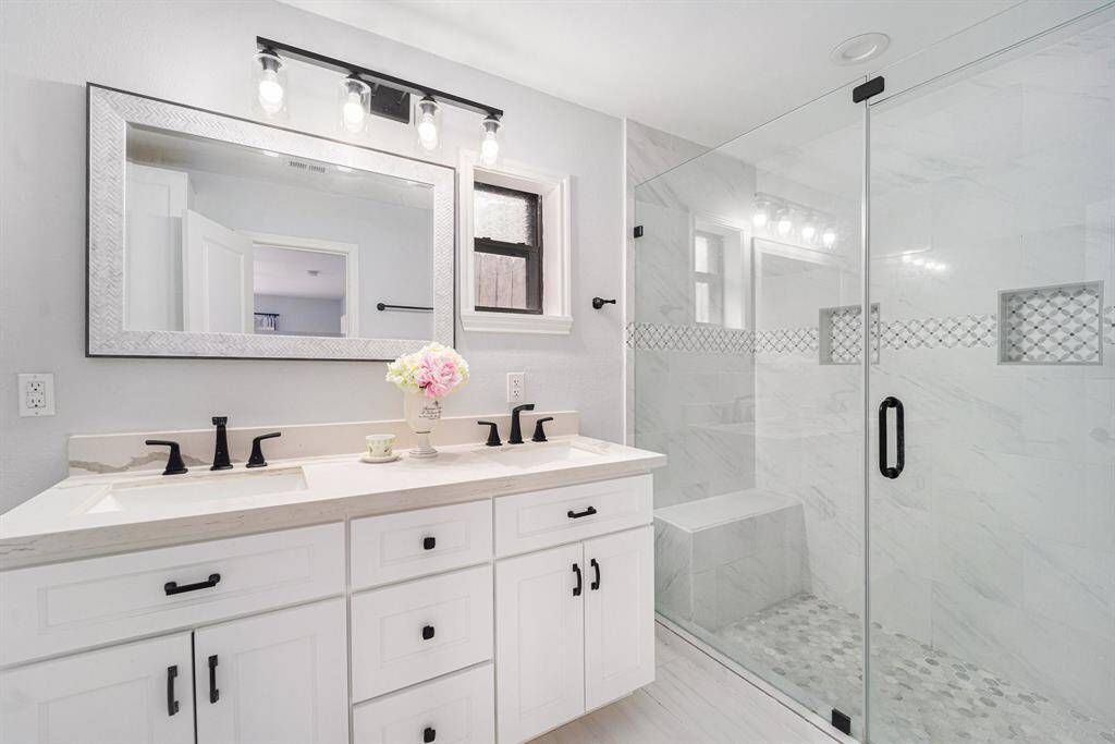 This modern bathroom features a dual-sink vanity with sleek black fixtures and ample storage.