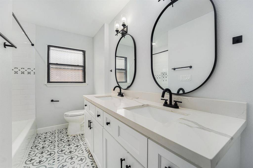 This full second bathroom with dual sinks, large round mirrors, and black fixtures,white cabinetry add a fresh, stylish touch.