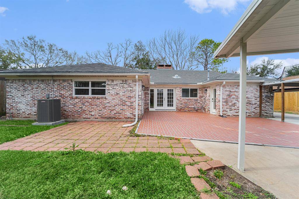 Large backyard with a mix of red brick and concrete pavers. There's a covered area providing shade, and the grass lawn adds greenery. French doors lead into the house, enhancing natural light and indoor-outdoor flow.