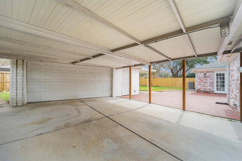 Covered carport with a concrete floor, adjacent to a brick exterior home, and the newly built fence for a fully fenced backyard.