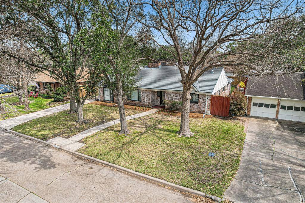 Charming single-story brick home with a spacious front yard featuring mature trees. The property includes a driveway leading to a two-car garage. Ideal for those seeking a cozy suburban setting.