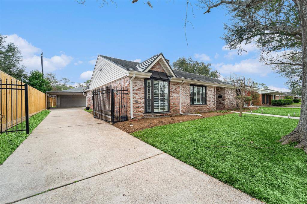 A spacious driveway leading to a detached garage, and a gated front entrance. The tidy lawn and mature trees add to its curb appeal, creating a welcoming atmosphere.