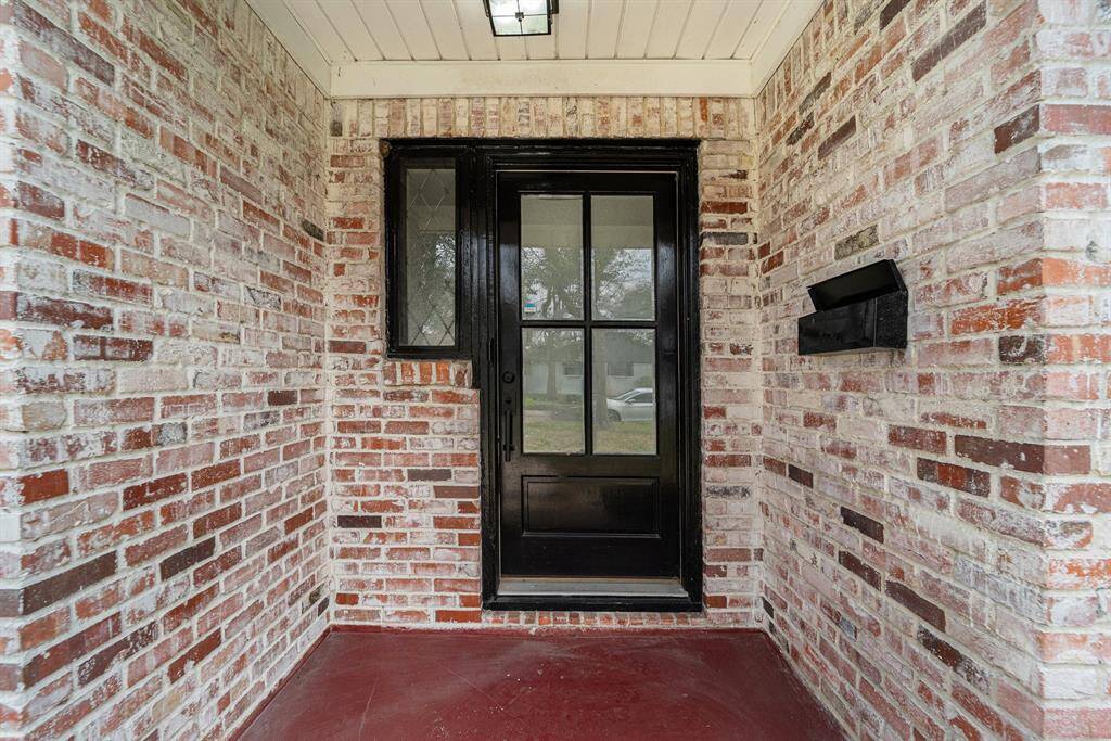 Brick entryway with a modern black door and side window, featuring a classic mail slot. Perfect for a welcoming first impression.