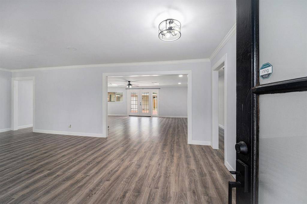 This photo showcases a spacious, modern open-concept living area with engineer wood floors and ample natural light. The room features a contemporary light fixture and leads to a set of French doors, enhancing the airy and inviting atmosphere.